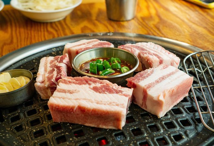 several raw pieces of pork belly on a grill